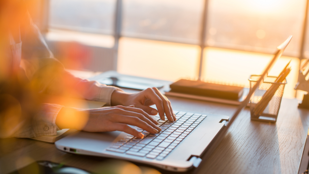 Business professional typing on a laptop in a sunlit office, researching invoice factoring solutions.